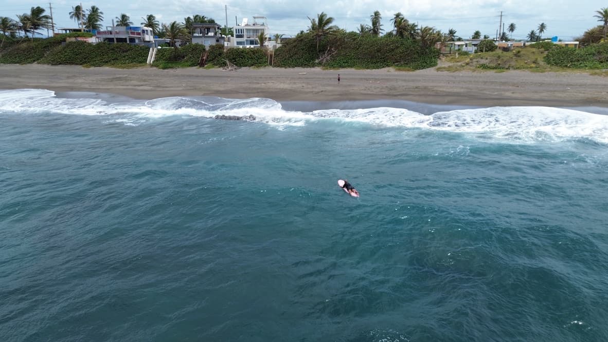 Ramon on his pink board with Arenas Negra and the black-sand beach behind him