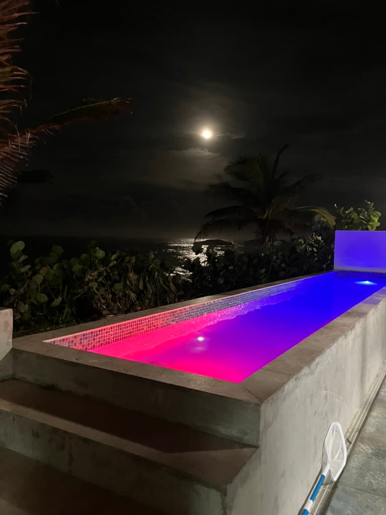 Full moon painting a silver path across the ocean beyond the pink and blue illuminated pool